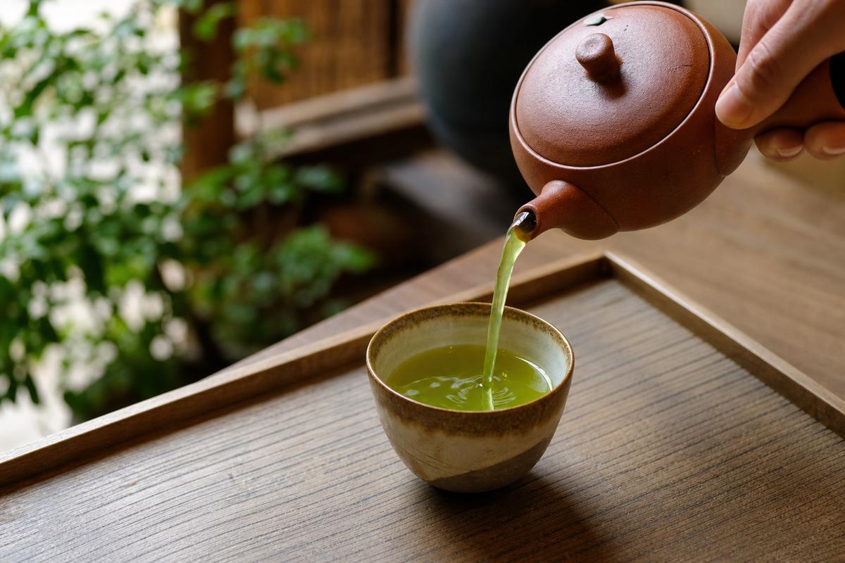 Green tea poured from a clay teapot into a cup